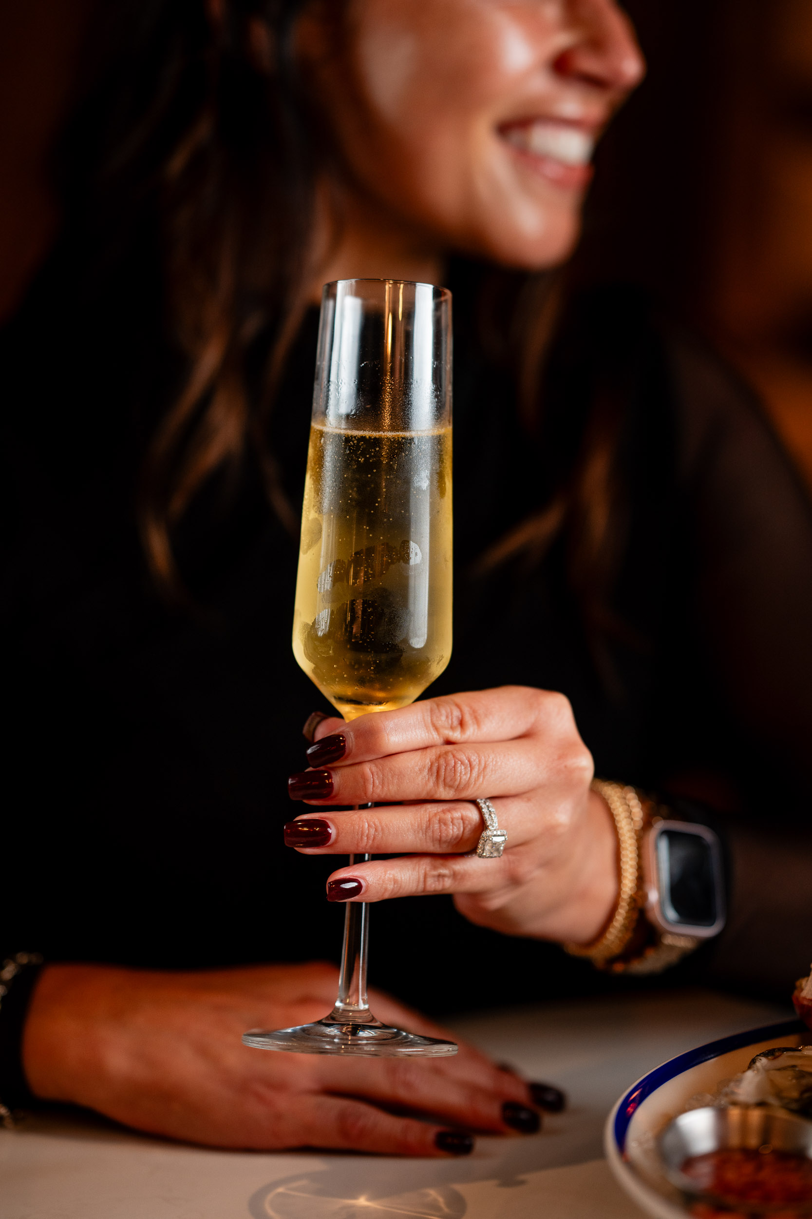 dark haired woman holds up champagne flute and smiles with a friend