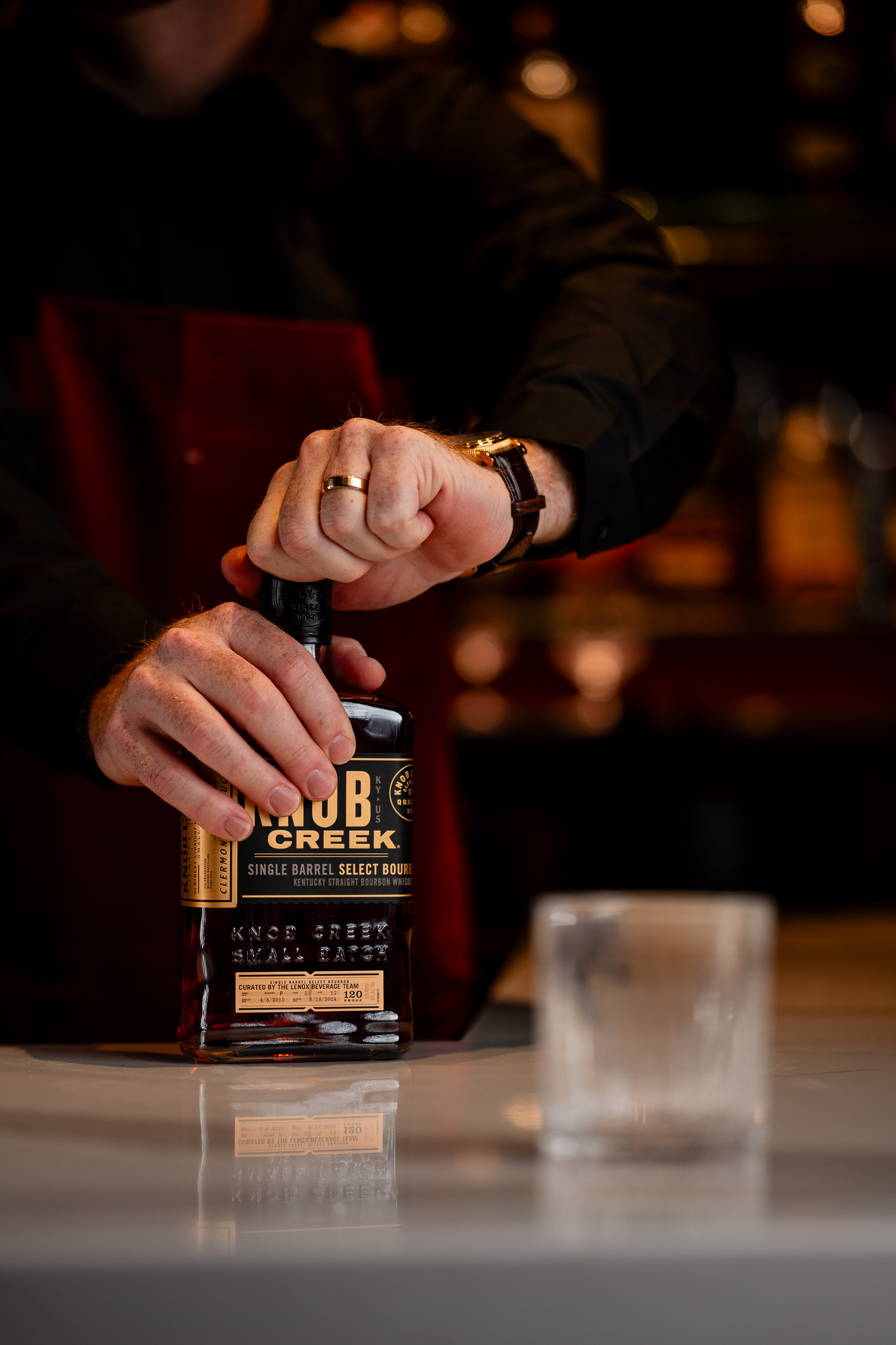 bartender twisting the cap off of knob creek bourban with a rocks glass in the foreground